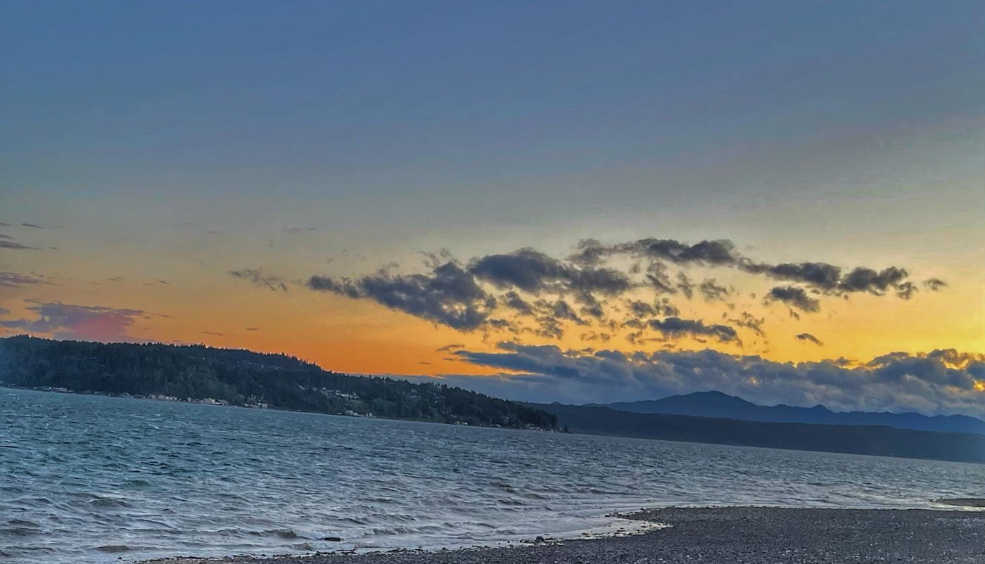Hood Canal at sunset in fall — driftwood on a pebble beach with orange sky over the Olympic Mountains